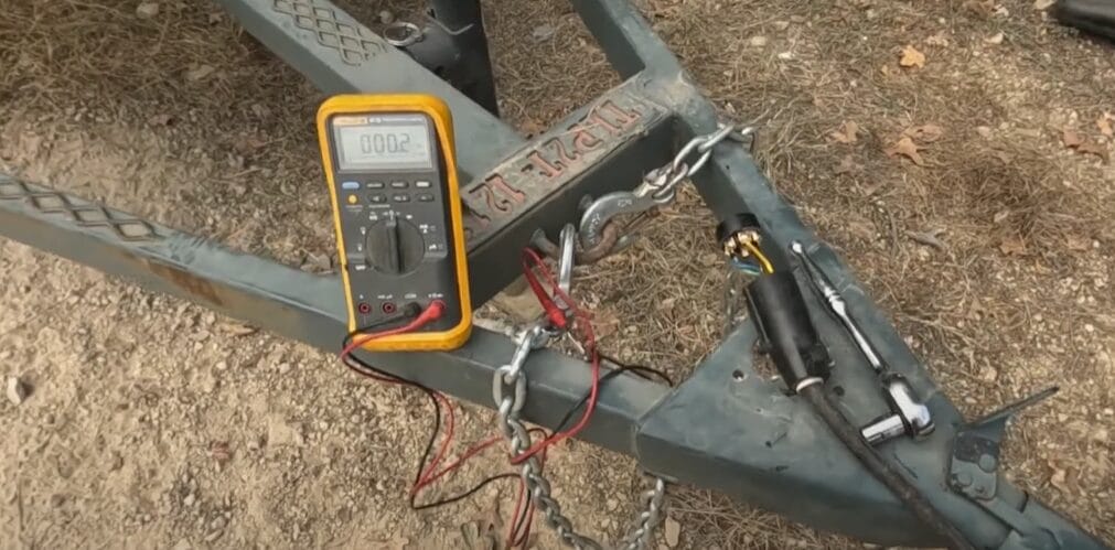 A yellow digital multimeter connected to trailer brakes using wires