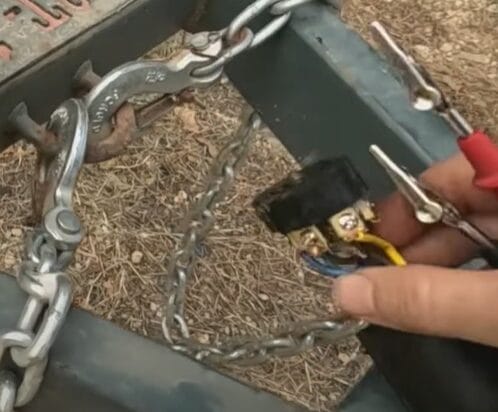 A person is using pliers to attach a chain to a trailer