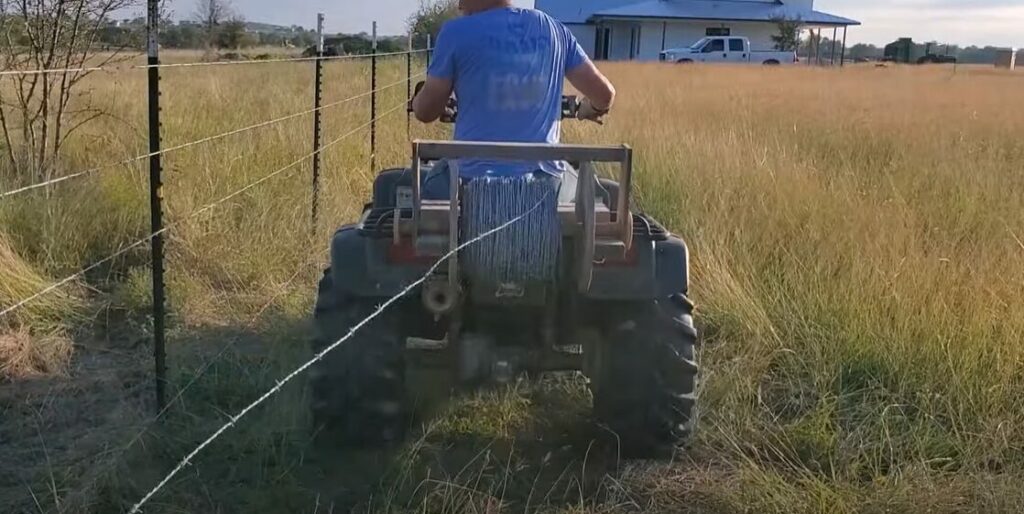 A man riding a four wheeler to install a wire fence on his farm