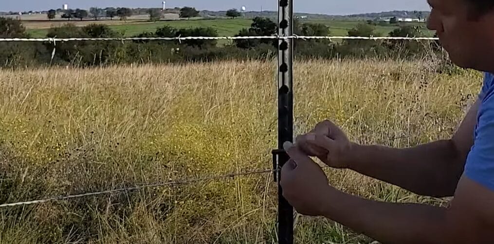 A man installing a T-Post clips on the wire fence