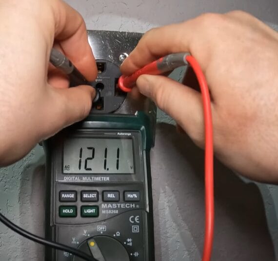 A person testing an outlet with 121.1 reading on the multimeter