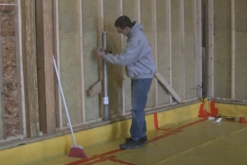 A man is carefully using a laser level to work on grading a wall in a house