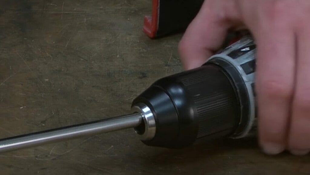 A person using a screwdriver on a table to remove a Milwaukee drill chuck.