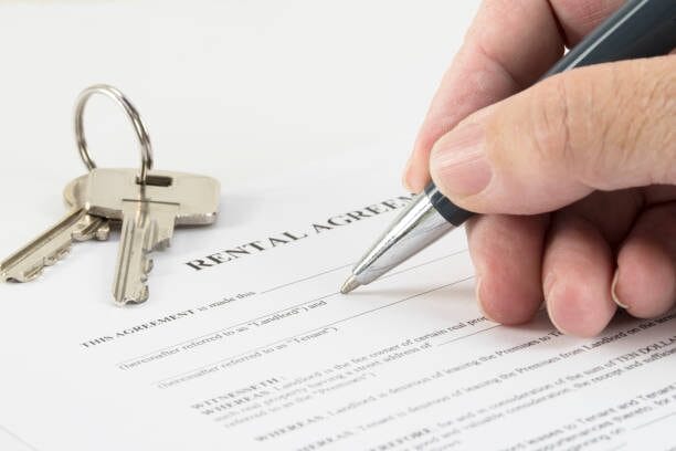 A person signing a rental agreement document with a key besides it