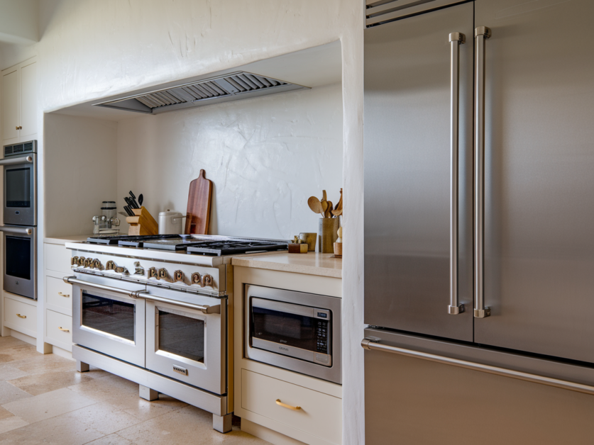 A modern farmhouse kitchen with stainless steel appliances, including a double-door fridge, a large gas stove with oven, a microwave, and various utensils on the countertop. Welcome to The Red Oak Retreat.