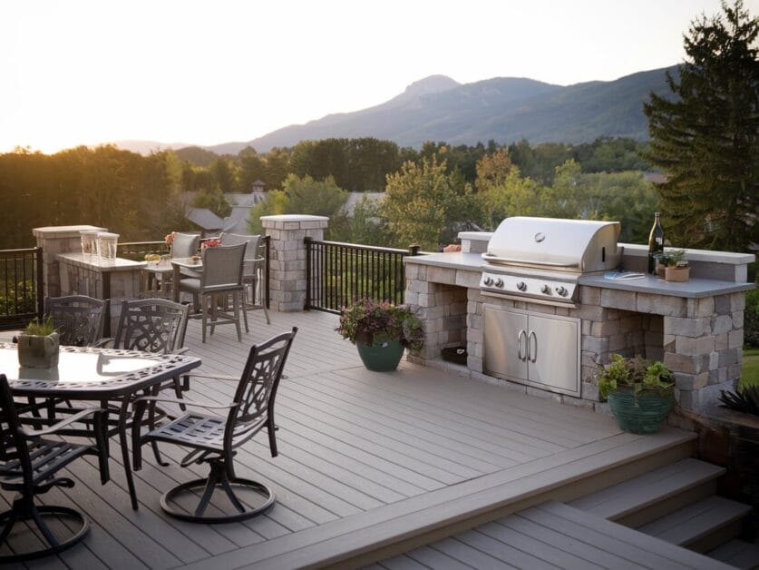 Dreaming of a perfect getaway? This spacious deck at the Ironclad Cabin features outdoor furniture, a built-in gas grill, potted plants, and a scenic mountain view surrounded by trees. Perfect for your 4-bedroom retreat.