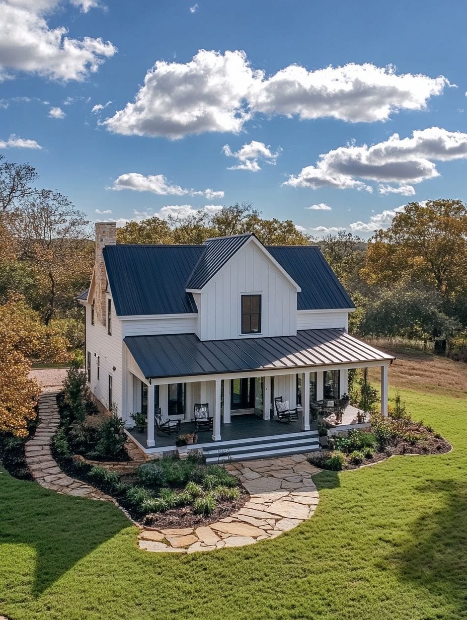 A two-story white farmhouse with a dark metal roof, wide front porch, stone pathway, and landscaped yard surrounded by trees under a blue sky with clouds.