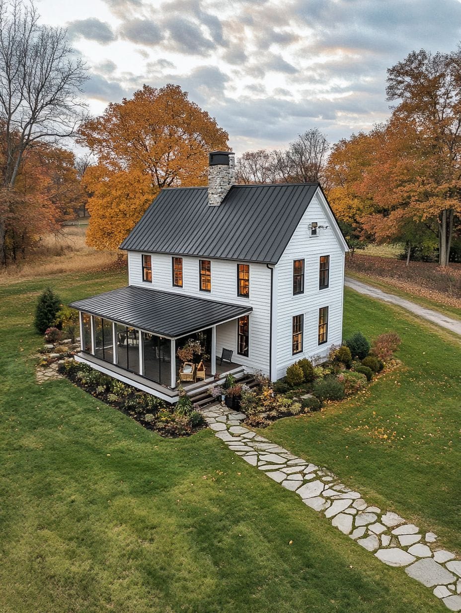 A white two-story house with a black roof sits among autumn trees, featuring a covered porch, stone pathway, and landscaped yard.