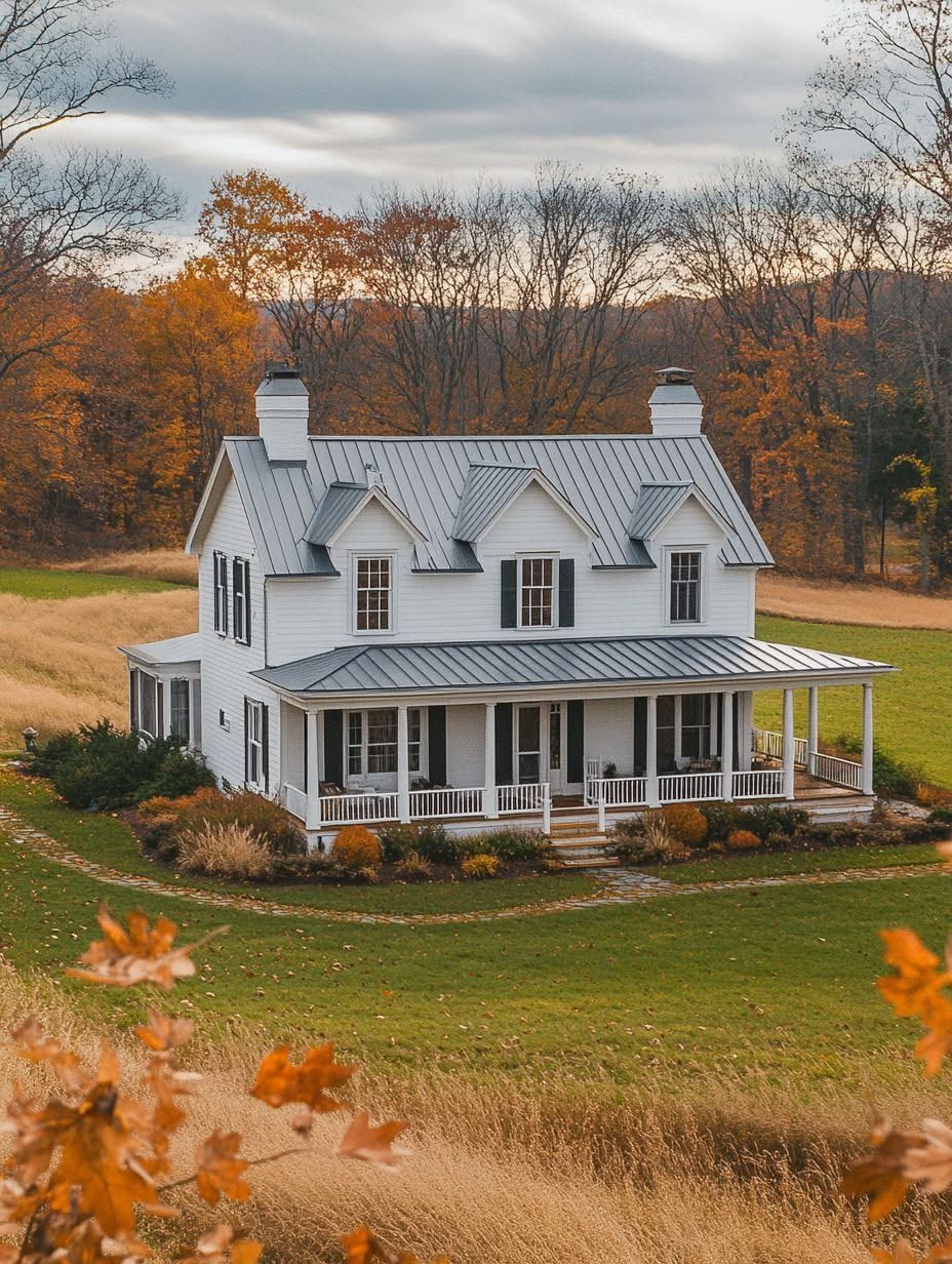 A white two-story house with a metal roof and wraparound porch sits in a grassy yard, surrounded by trees with autumn foliage.