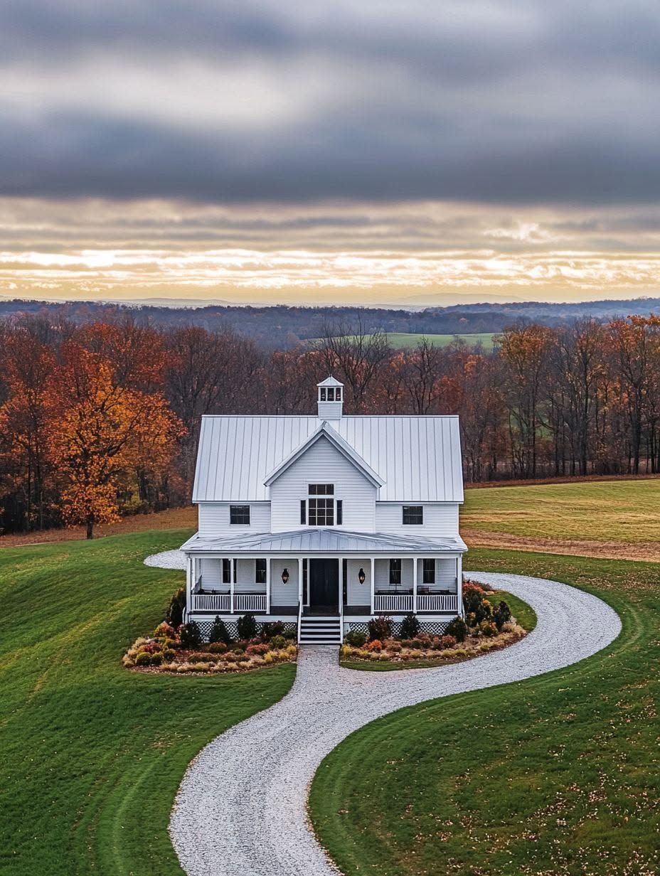A white two-story farmhouse sits in a large, grassy yard with a curved gravel driveway and autumn trees in the background under a cloudy sky.